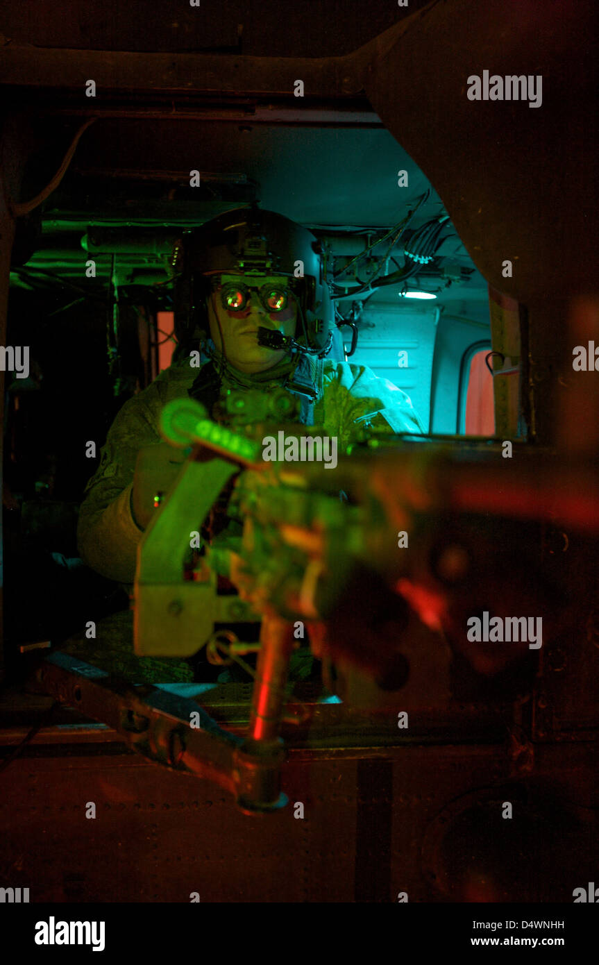 Crew cheif equipped with night vision goggles mans a M240G machine gun aboard a UH-60 Black Hawk helicopter. Stock Photo