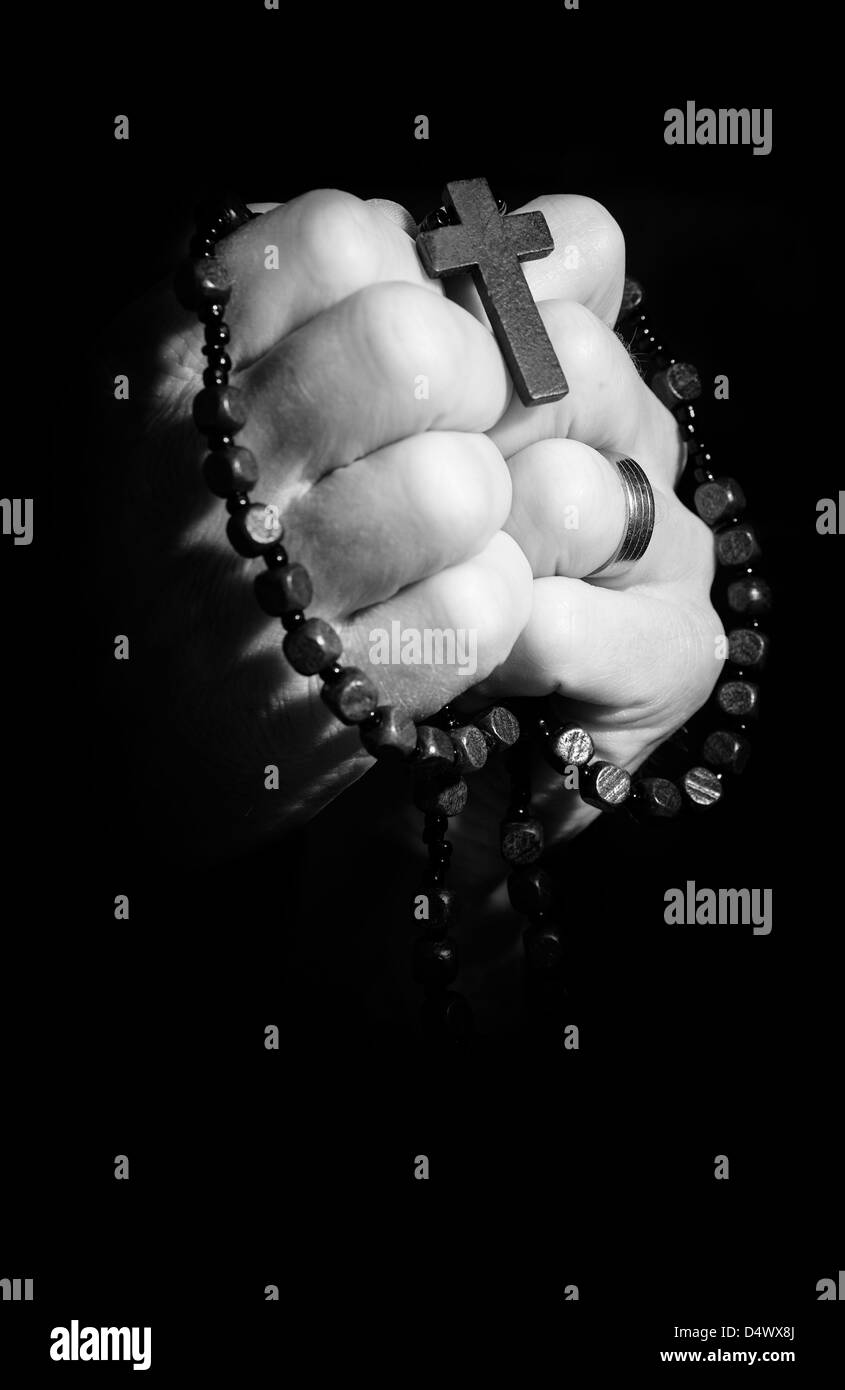 Hands holding onto rosary beads and cross while praying Stock Photo Alamy