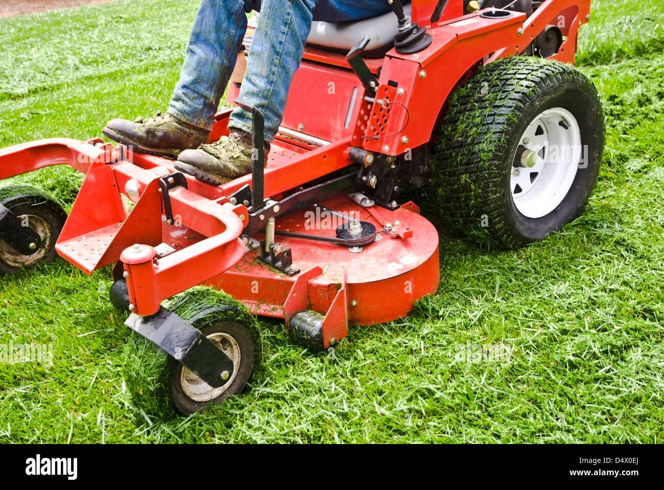 Man on a riding lawn mower that has grass stuck to the wheels. Spring and summer outdoor maintenance. Stock Photo