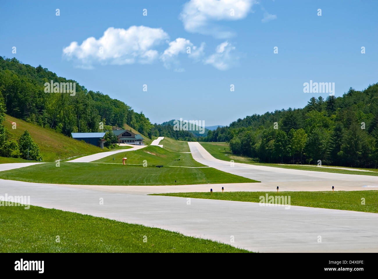 A small private airport runway, with a road intersecting it, in the north Georgia mountains, buildings in the distance. Stock Photo