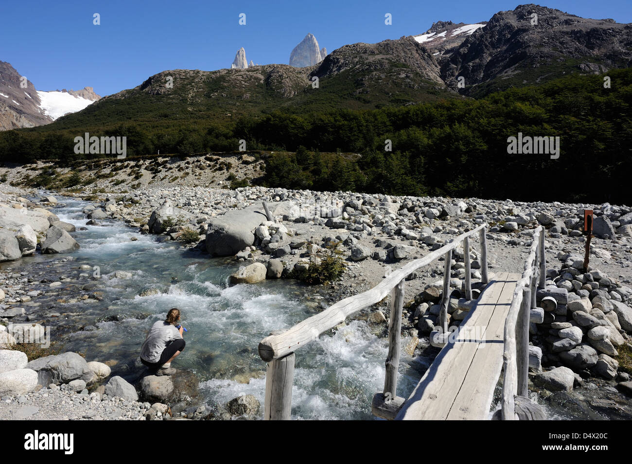 A walker fills her water bottle by a bridge over a stream in Los Glaciares National Park at the foot of the Fitzroy Range Stock Photo