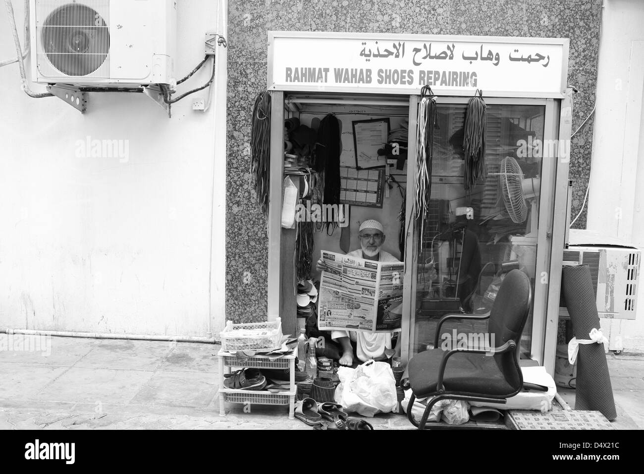 Man sitting in small shoe repair booth, Dubai, United Arab Emirates Stock Photo