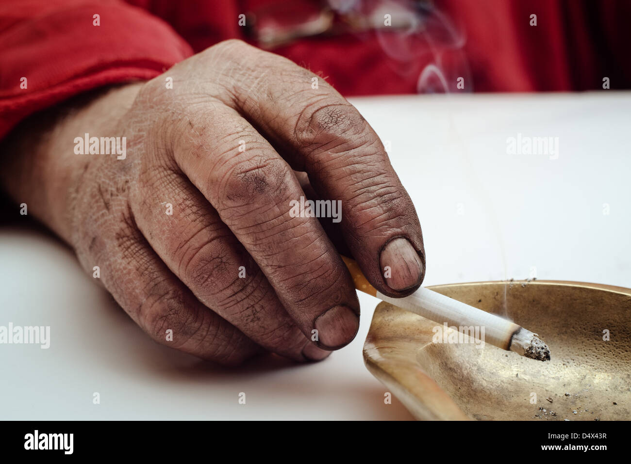 Dirty male hand holding smoking cigarette in an ashtray. Stock Photo