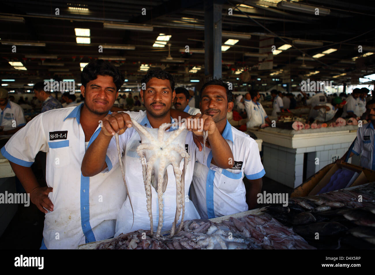 Three men pose for photo with octopus at market in Dubai, United Arab Emirates Stock Photo