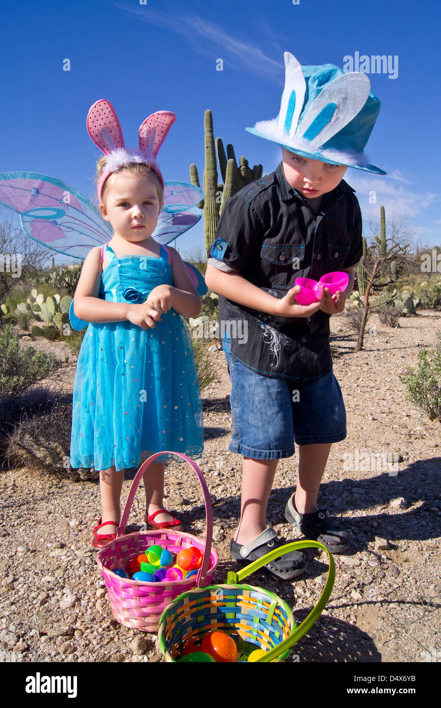 5 year old brother and 3 year old sister having fun on an easter egg hunt in the desert wearing hats and butterfly wings. Stock Photo
