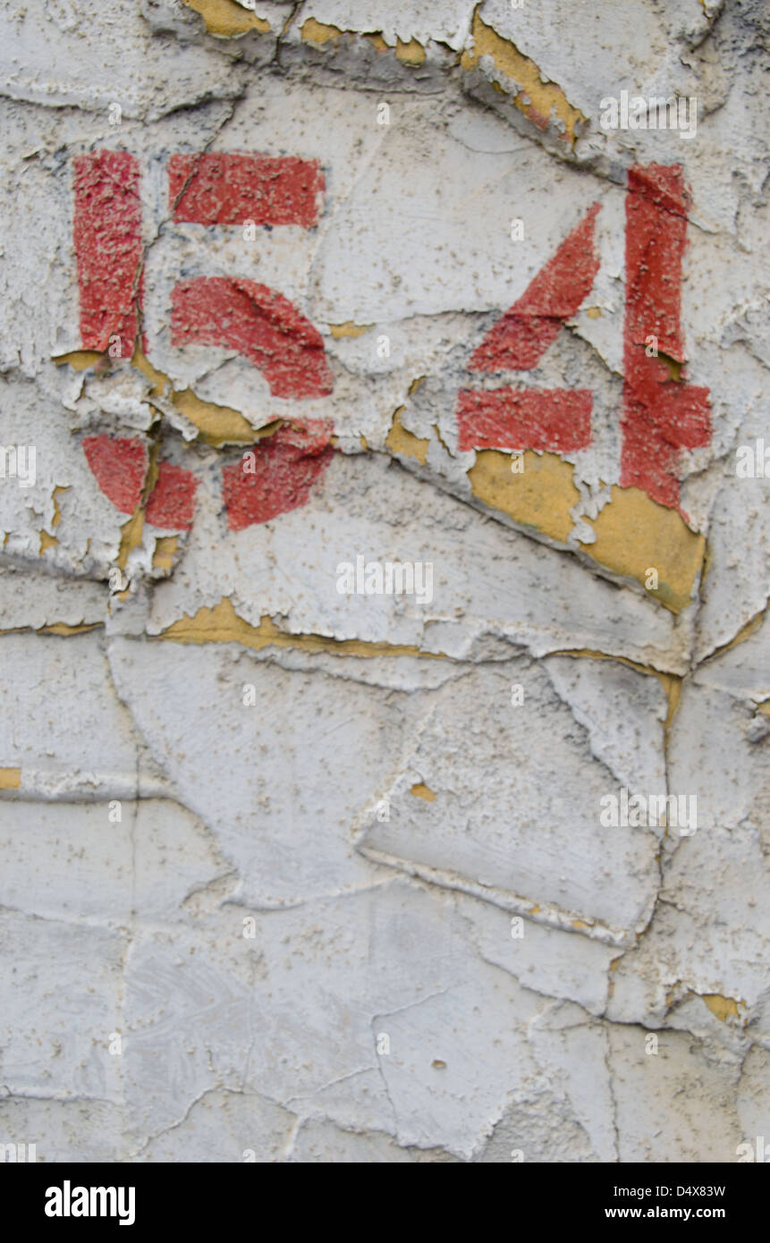 Abstract, gritty, urban background texture featuring a stenciled, painted '54' on a peeling white cement wall in Pittsburgh Stock Photo