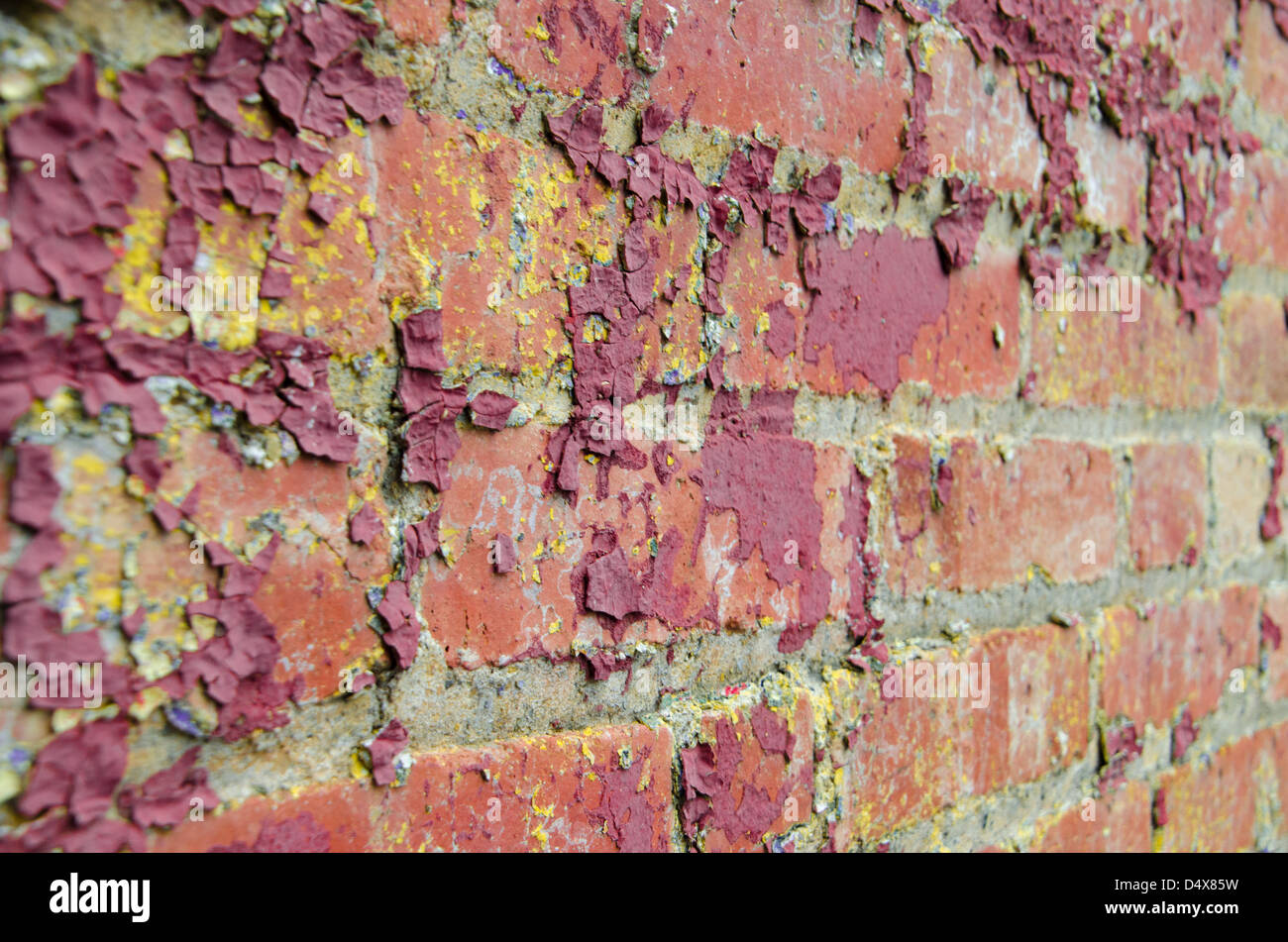 Gritty urban background red brick wall texture with peeling dark red paint and yellow splatters Stock Photo