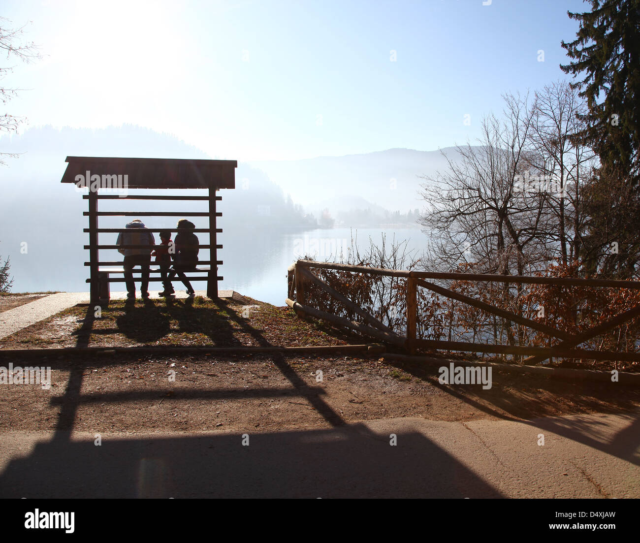 Silhouette of a family of mother and father and son on a wooden bench on a misty morning at Lake Bled Slovenia Stock Photo