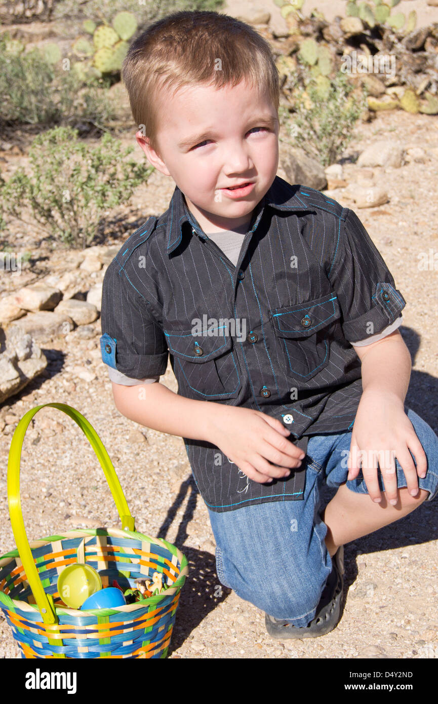 A five year old boy crouches without sitting directly on the sandy desert ground. Stock Photo