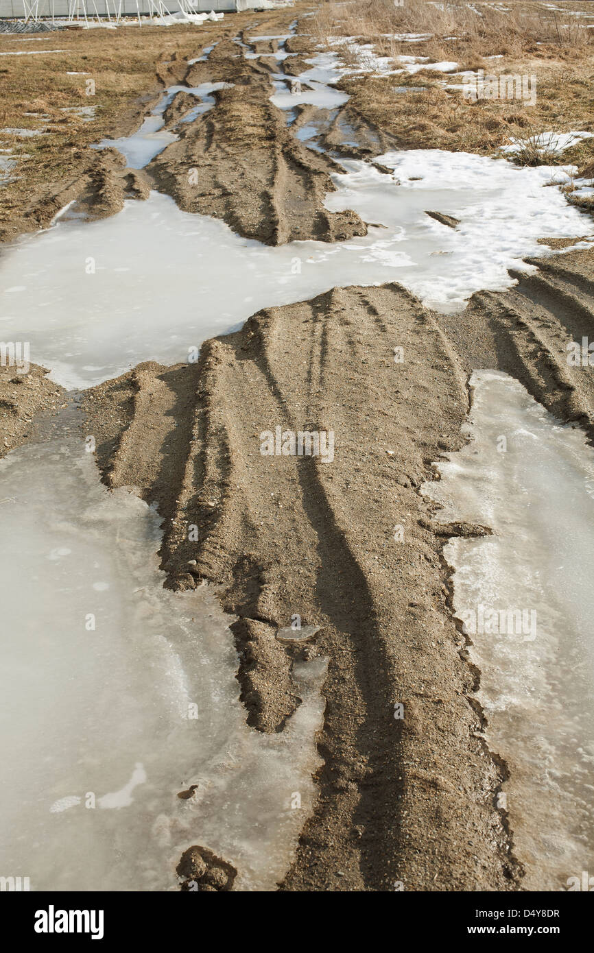 Late winter dirt road shows deep ruts and ice that has collected. Stock Photo