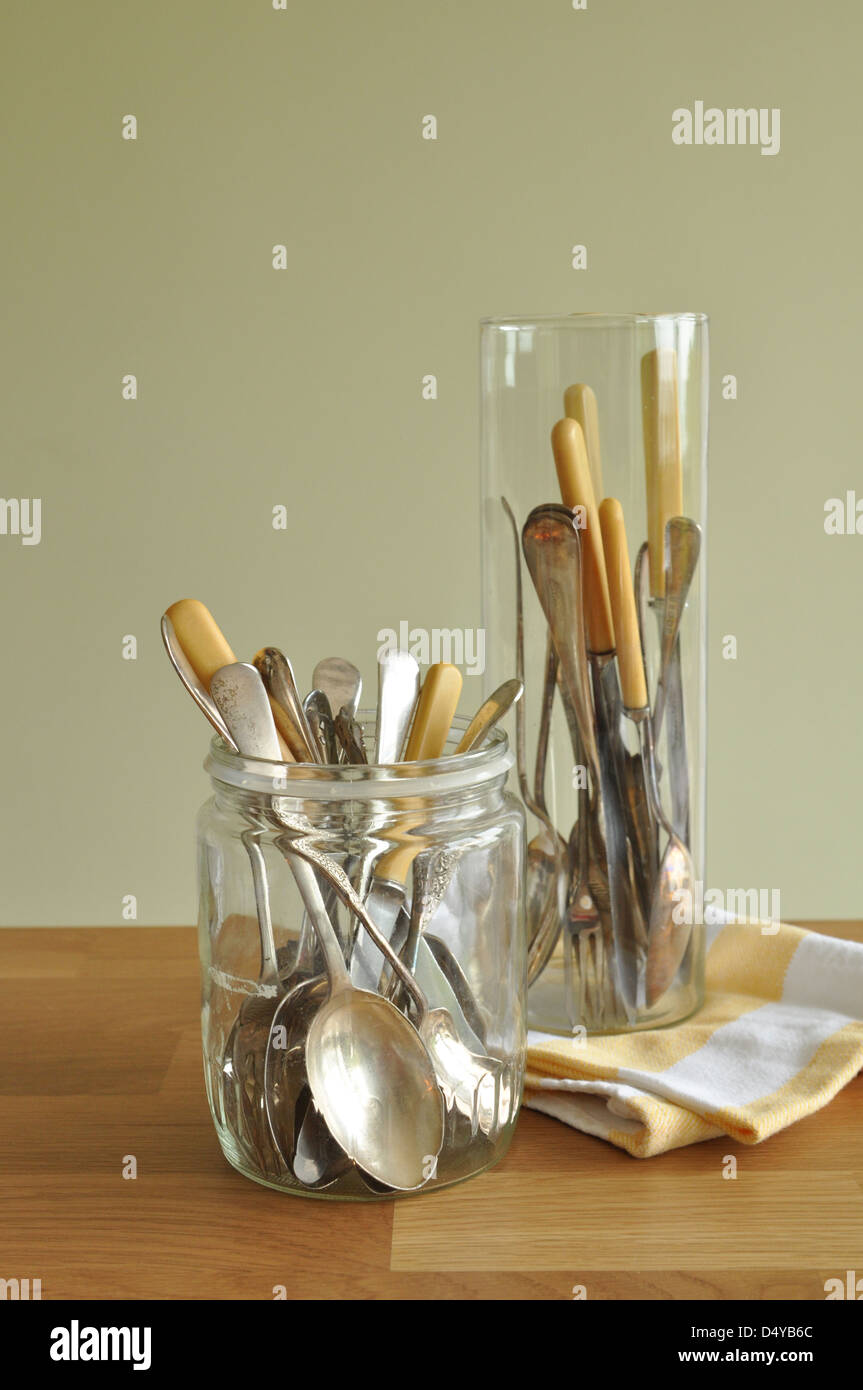 Vintage cutlery silver with bone handles in glass jars on wooden table with vintage yellow tea towel on green Stock Photo
