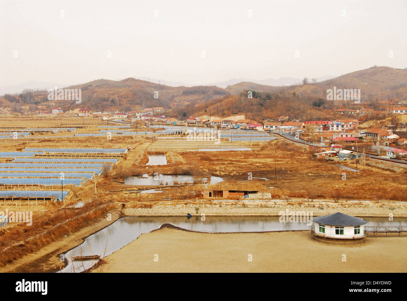 China, Dandong, elevated view of a salt pond with human settlement and mountains in the background Stock Photo