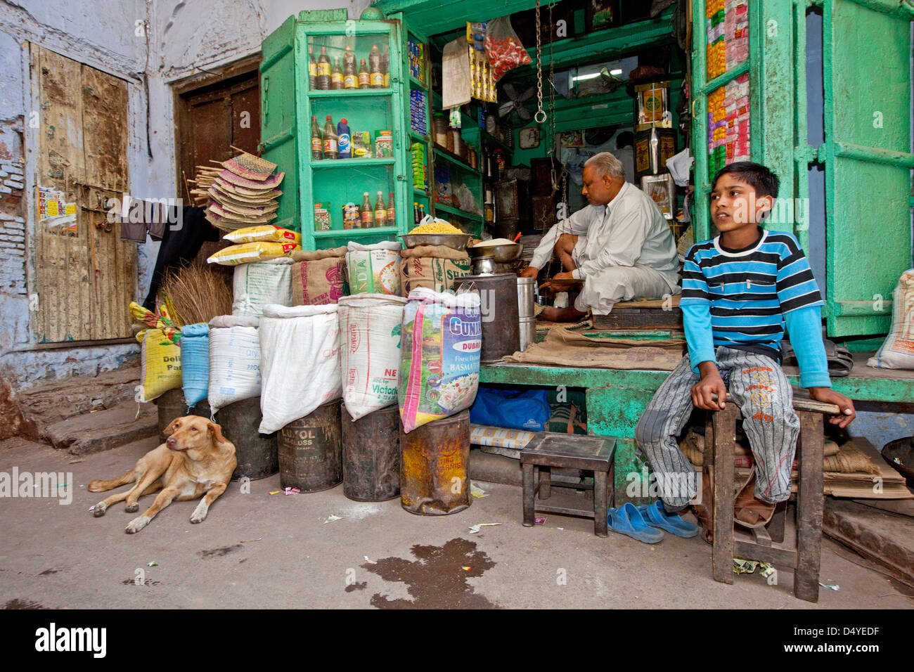 A small merchant in Delhi keeps shop with his son and dog, India. Stock Photo