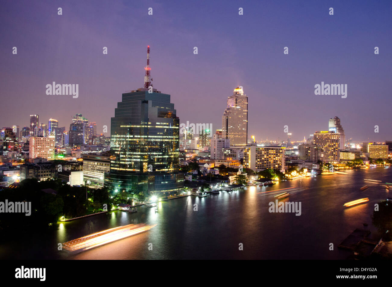 Thailand, Bangkok. Downtown Bangkok, evening skyline view of the Chao Phraya river waterfront with lighted boats. Stock Photo
