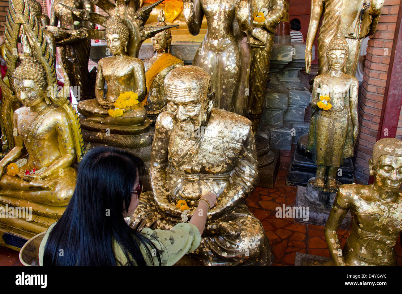 Thailand, Ayutthaya. Wat Phra Chao Phya-thai. Temple visitors place small gold leaf squares on Buddha statues as offering. Stock Photo