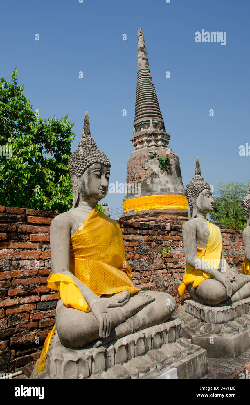 Thailand, Ayutthaya. Wat Phra Chao Phya-thai. Seated Buddha statues dressed in yellow robes, bell-shaped Chedi temple. UNESCO Stock Photo