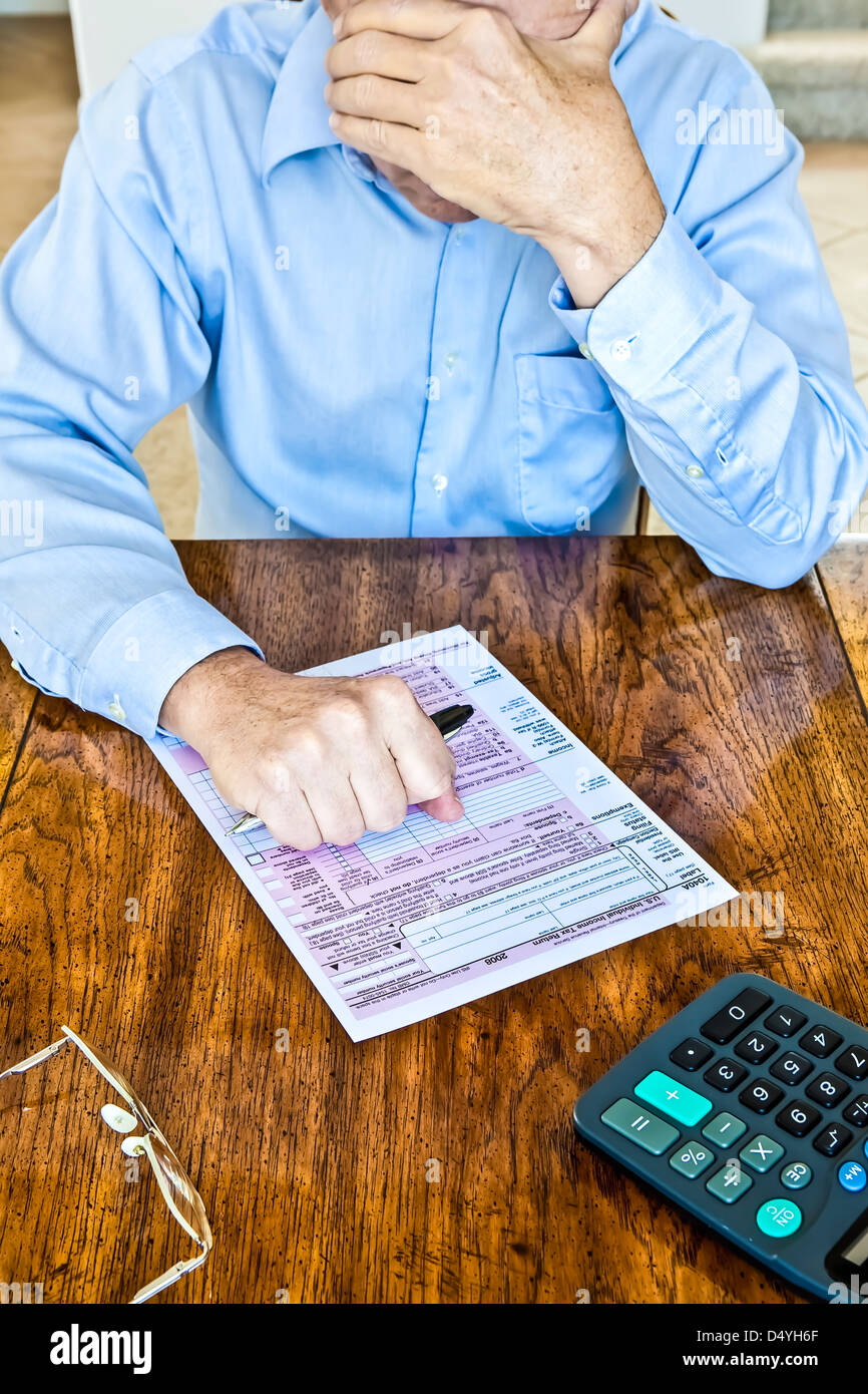 Older man with age spots on hands with US Federal tax form on wooden table with pen in clenched fist and calculator Stock Photo