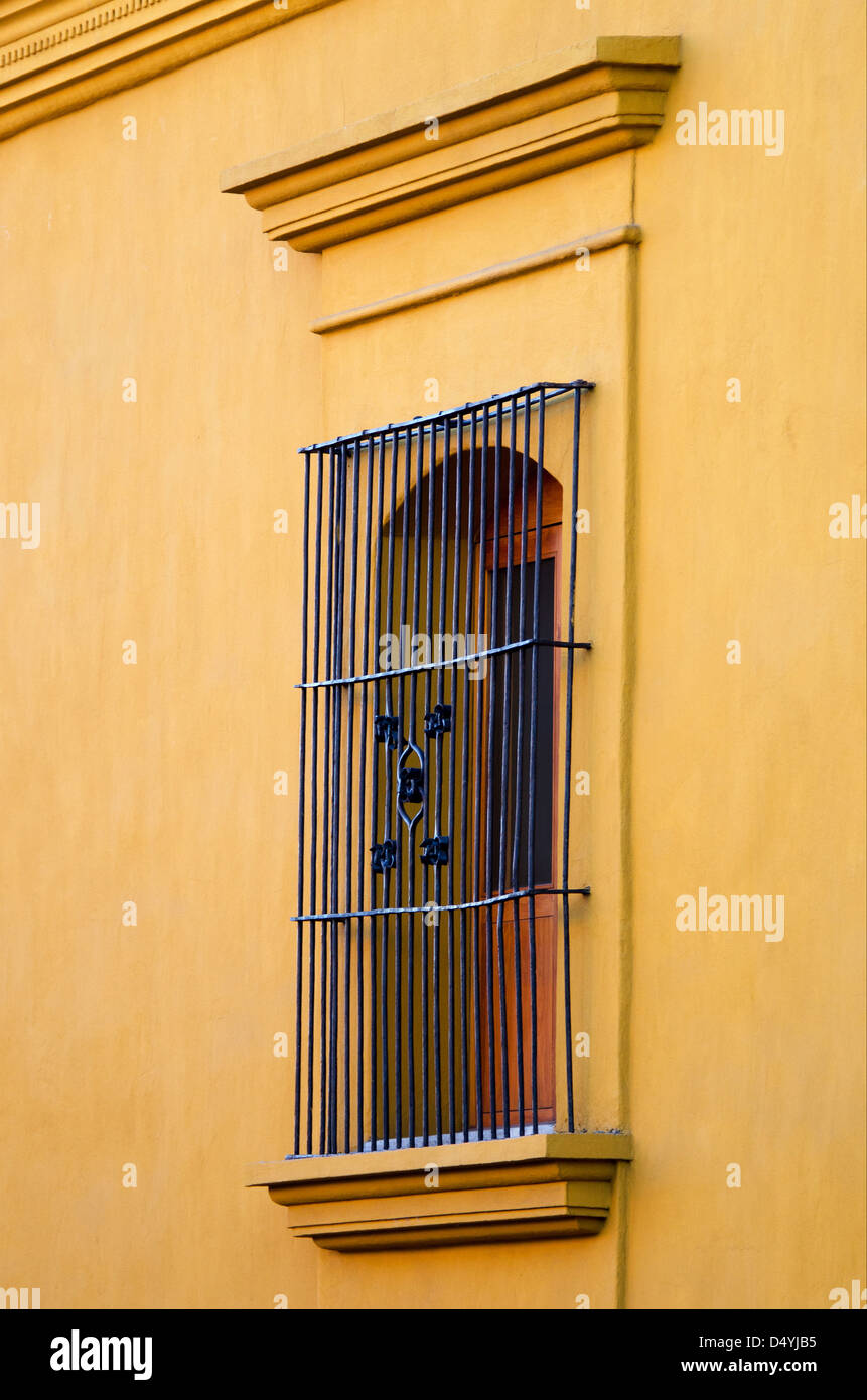 A decorative wrought iron security grill guards an arched window in a saffron yellow plaster wall, Oaxaca, Mexico. Stock Photo