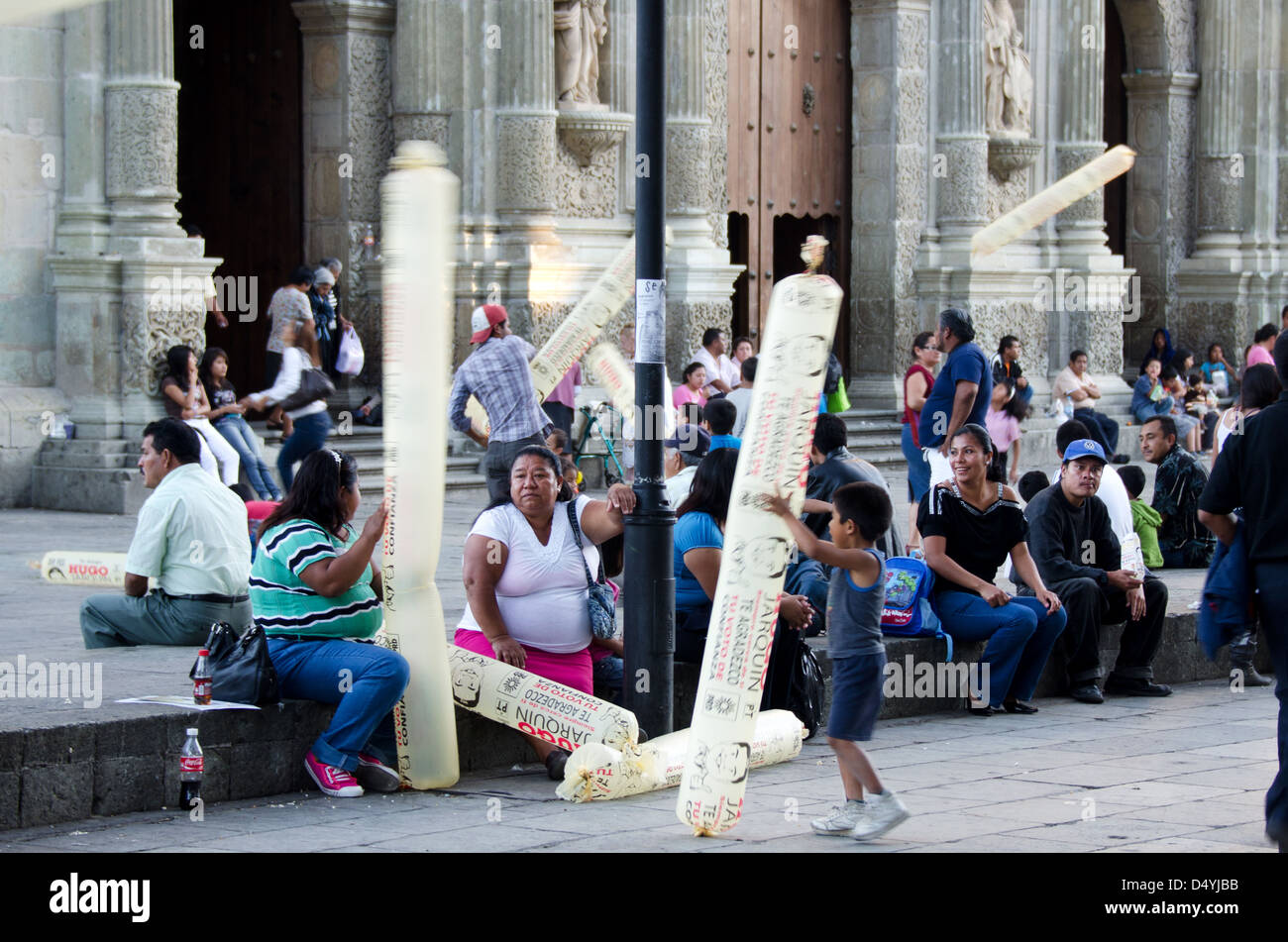 Children play with inflatable political advertising toys as adults talk and watch the street life in the Zócalo, Oaxaca, Mexico. Stock Photo
