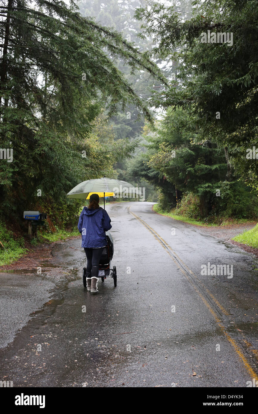 a woman pushing a stroller on a road on a rainy day. Stock Photo