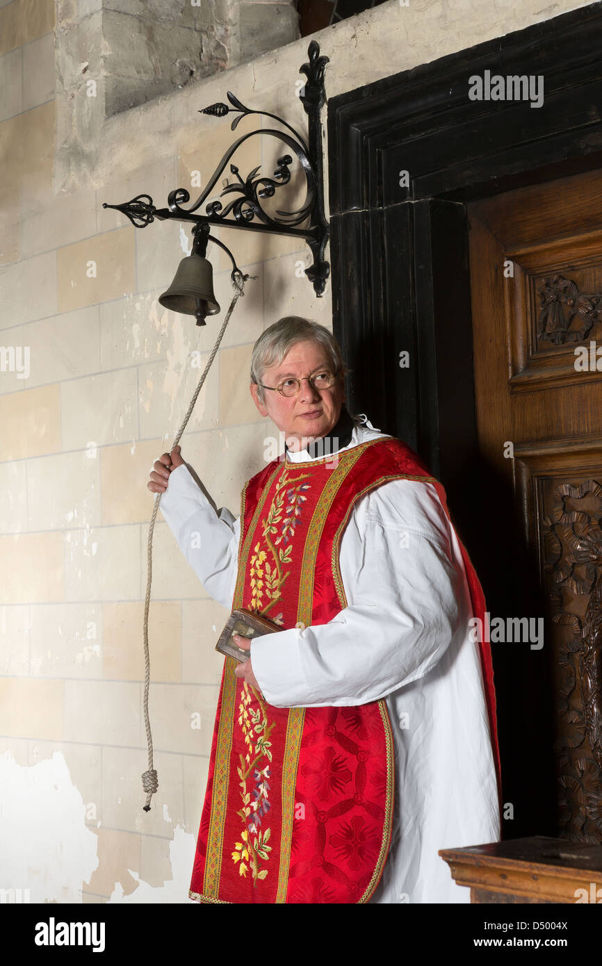 Catholic priest entering the church and ringing the bell for the beginning of mass Stock Photo