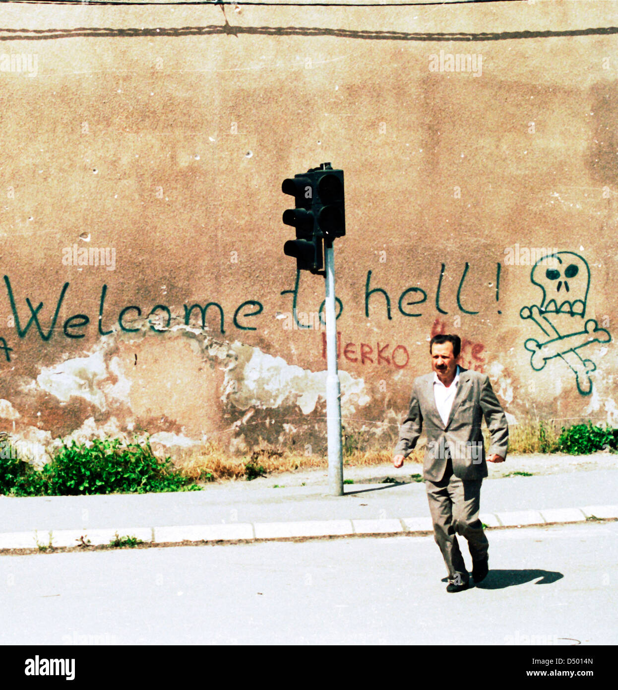 A man braves sniper fire as he runs past a graffiti scrawl that reads 'Welcome to Hell' in Sarajevo, Bosnia, on Monday, May 31, 1993. Stock Photo