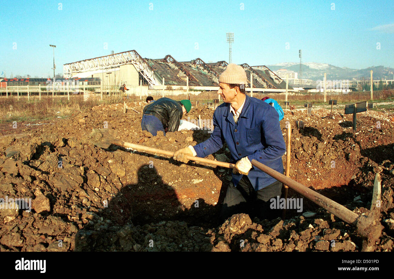 SARAJEVO, BOSNIA, 01 MARCH 1994 --- Grave diggers prepare more graves for the victims of Bosnia's civil war. Behind them stand the ruins of the 1984 Olympic stadium and ice arena. Stock Photo