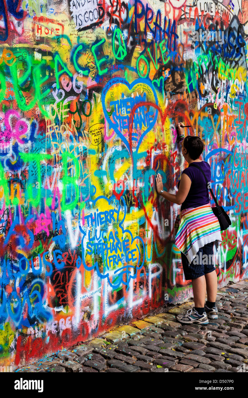 A young tourist girl adds graffiti to the John Lennon Wall in Prague, Praha, Czech Republic,Česká Republika,Europe Stock Photo