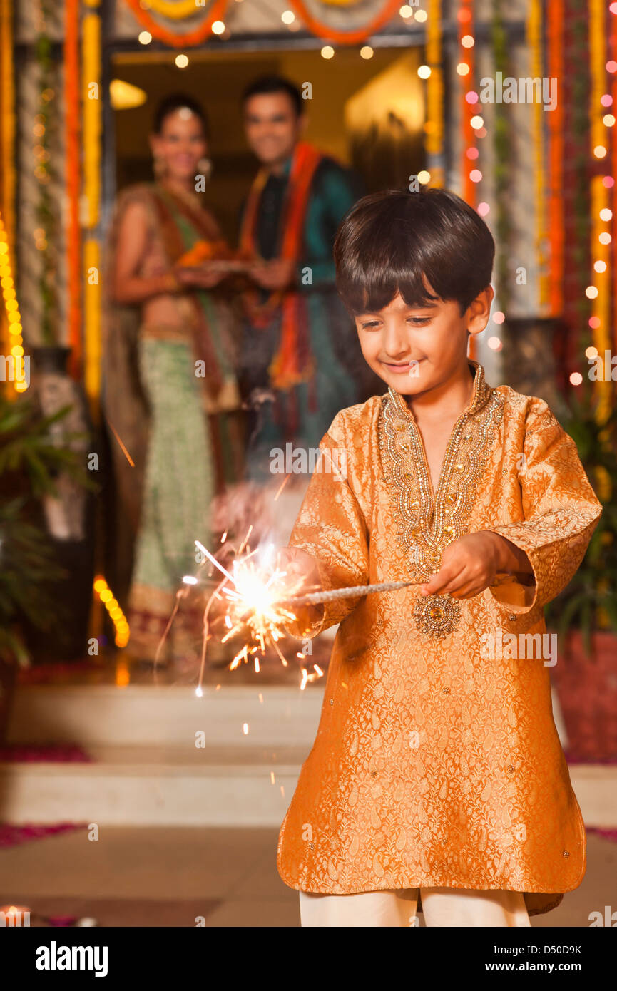 Boy burning fire crackers with his parents in the background on Diwali
