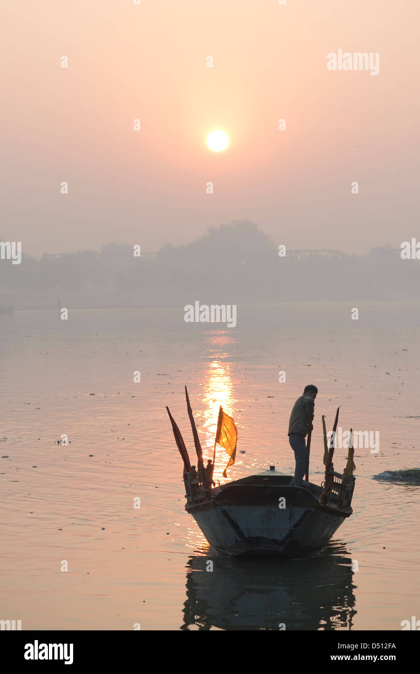 A boatman steers his boat as the sun rises over the Yamuna river at Vishram Ghat, Mathura, Uttar Pradesh, India Stock Photo