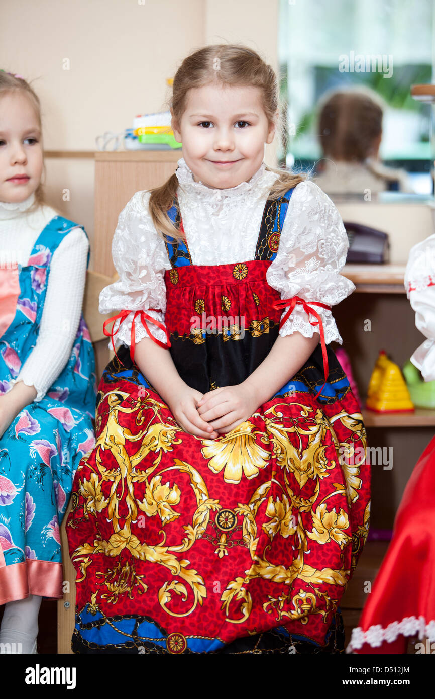 Cute girls in Russian traditional clothes in kindergarten sitting on the chairs in classroom