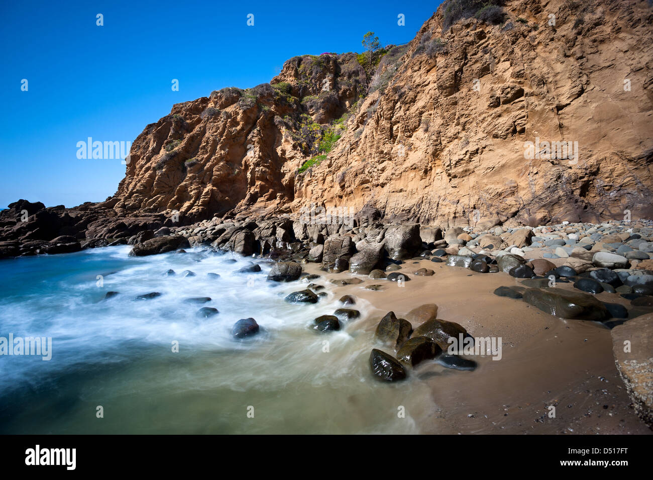 A secluded cover in Laguna Beach, California shows the seawater rushing to shore over smooth boulders. Stock Photo