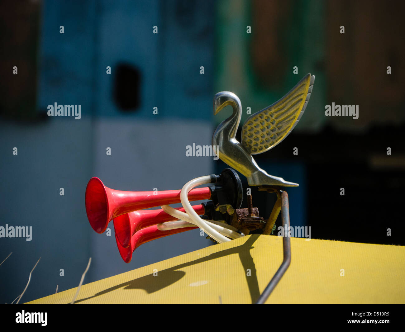 Metal swan hood ornament and three red plastic air horns on a car hood
