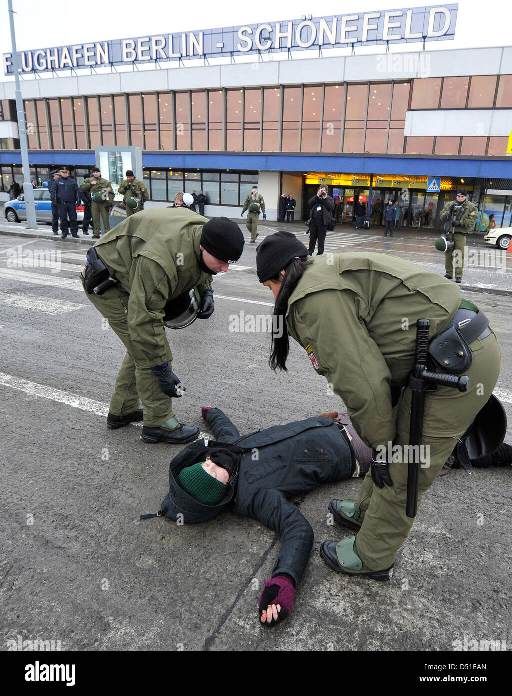 Police officers prepare to carry away a demonstrant lying on the street during a protest action at the Berlin airport in Schoenefeld, Germany, 6 December 2010. Adolescents protest against the planned deportation of a Vietnamese in front of the airport. Photo: Bernd Settnik Stock Photo