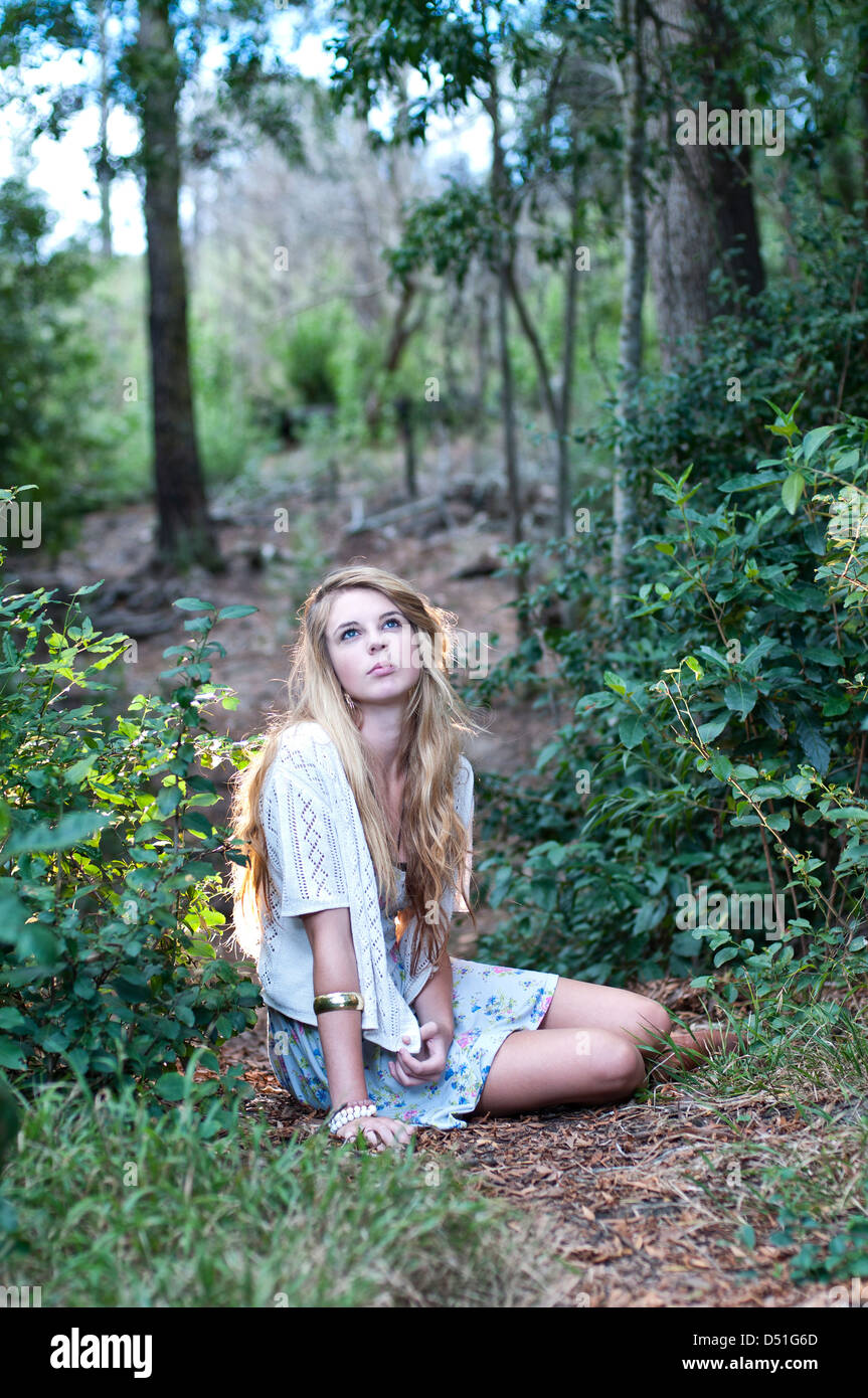 Sexy young Caucasian girl with short dress sitting on the forest floor staring up to the trees. Stock Photo