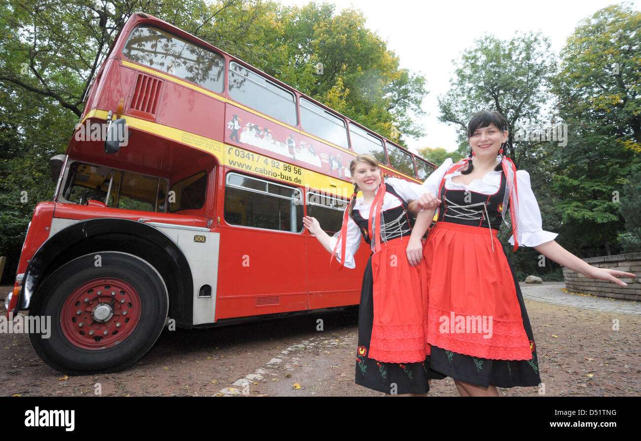 Models Nicole Schiertz (L) and Anne Bibas stand in front of an English double-decker bus, dressed in traditional Swiss clothes in Leipzig, Germany, 29 September 2010. On the same day, the TMS Fair-Congress and Exhibition GmbH informed visitors on the International Tourism and Caravaning Fair, taking place from 17-21 September 2010 in Leipzig. More than 1000 international and nation Stock Photo