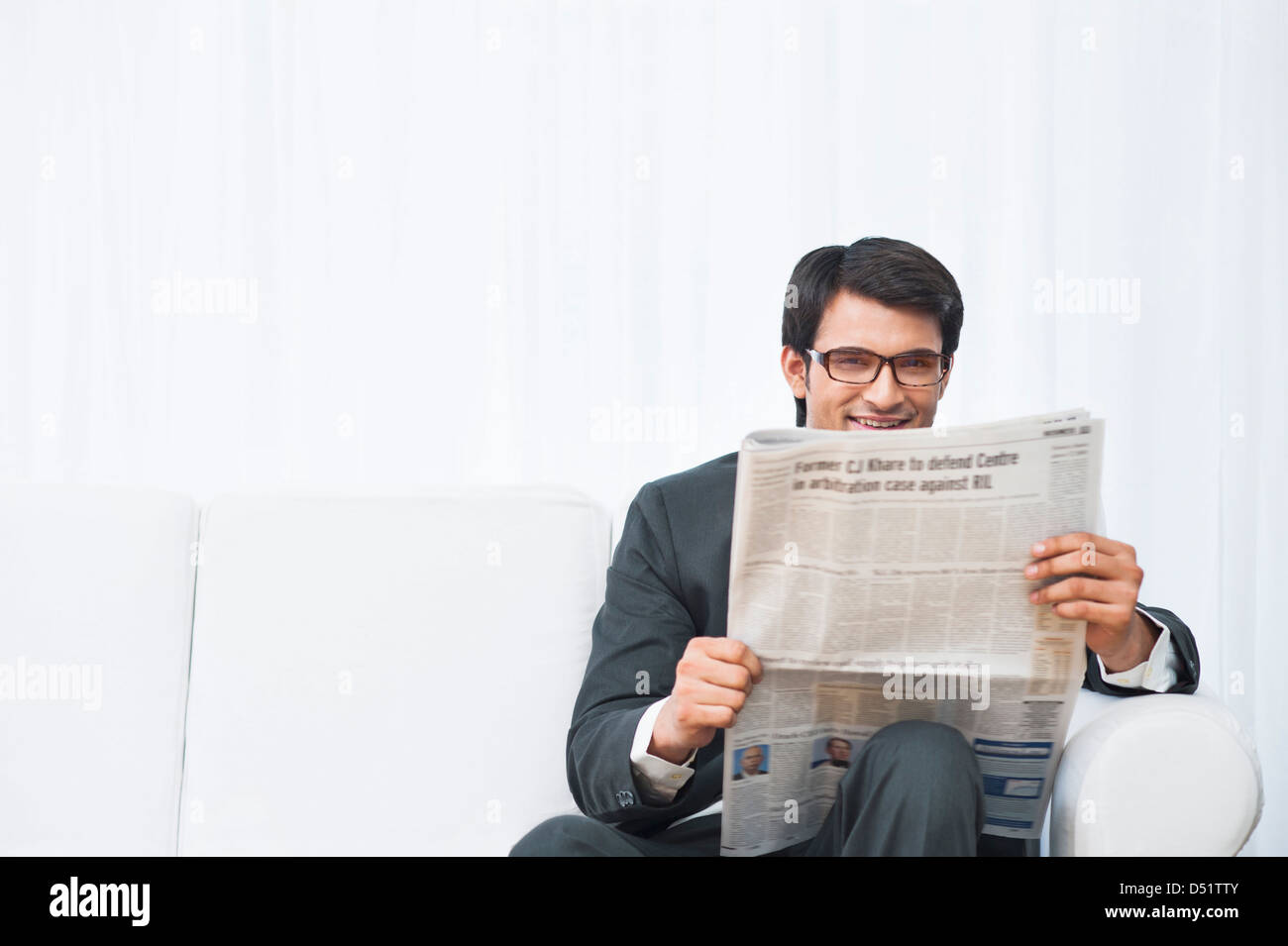 Businessman sitting on a couch and reading a newspaper Stock Photo - Alamy