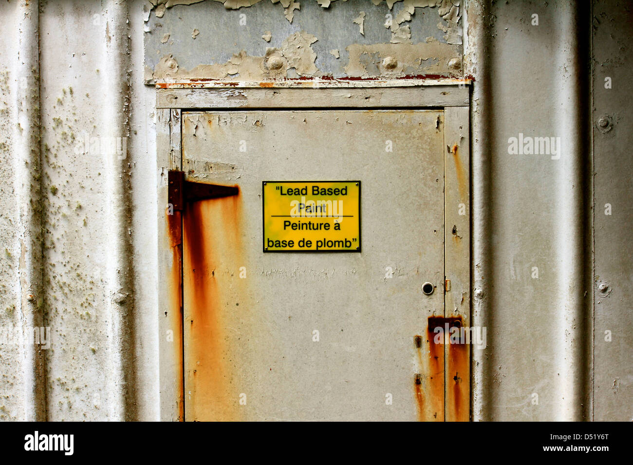 Bright yellow 'lead based paint' sign in French and English on a door with rusty hinges and peeling paint Stock Photo