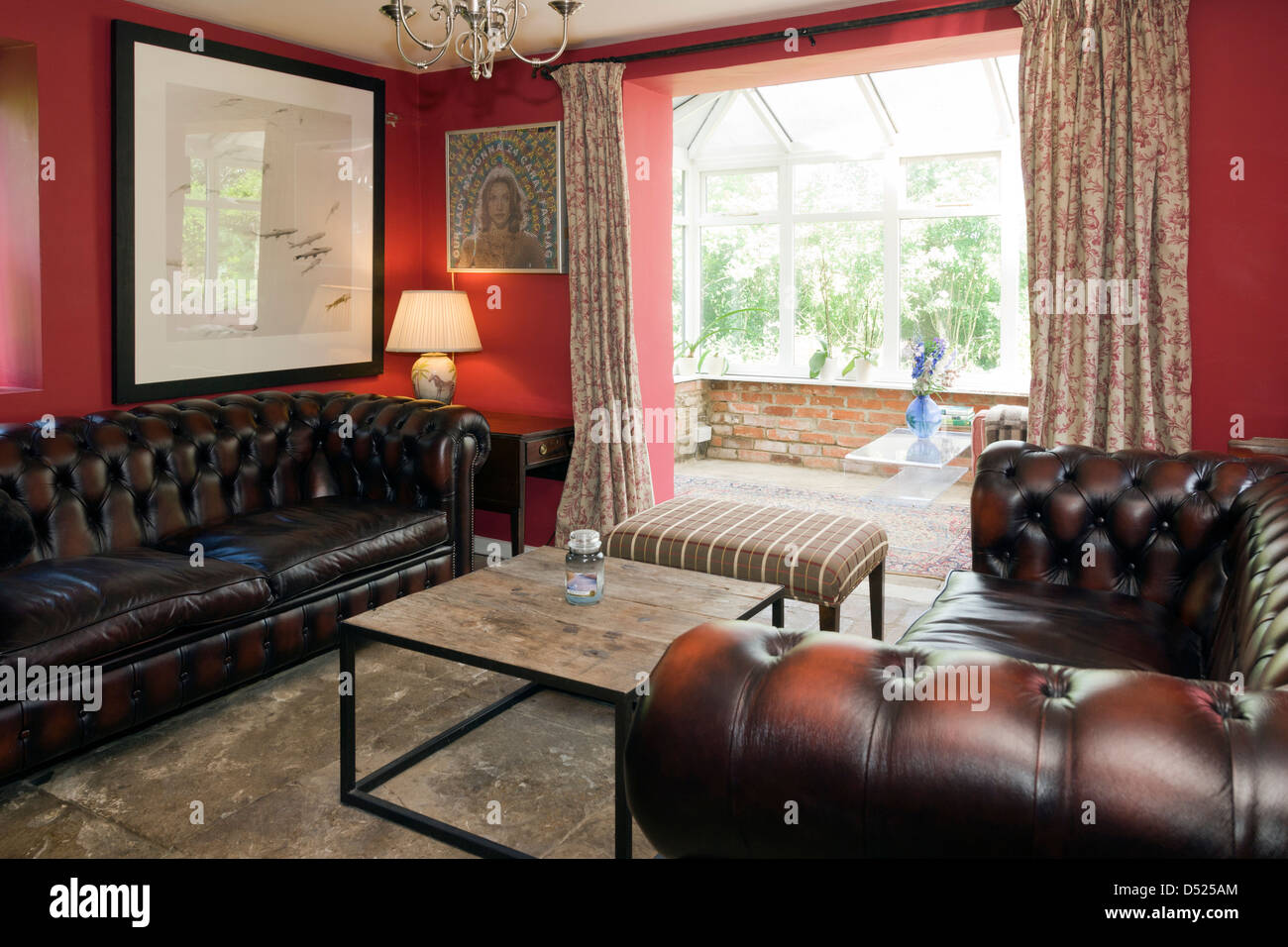 Two leather sofas in a red painted sitting room with conservatory