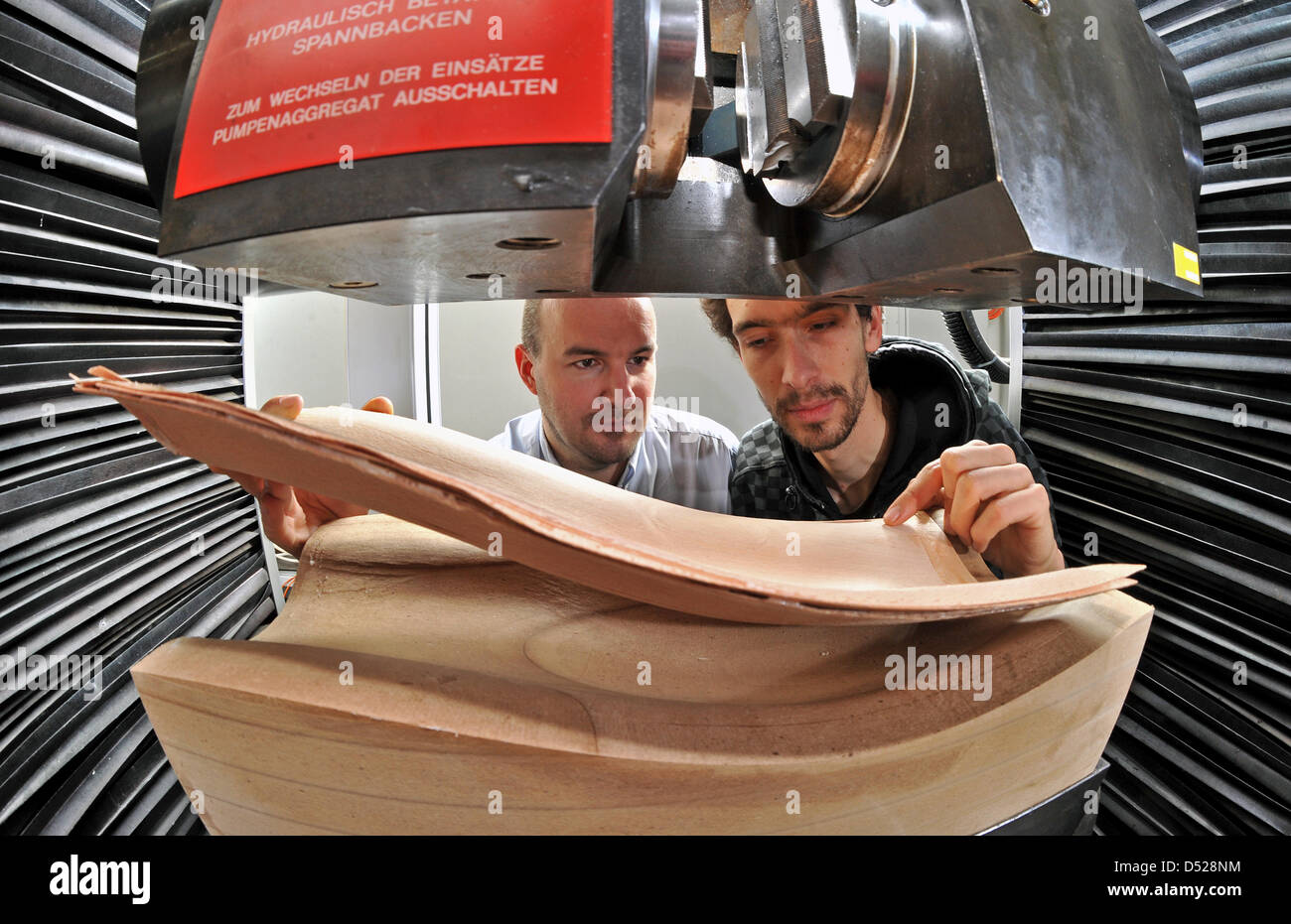 Chartered engineer Lars Ehlers (L) and student Martin Hegenbarth (R) inspect a wood shaped part in Leipzig, Germany, 25 October 2010. Scientists of Civic Engineering faculty of Leipzig University of Applied Sciences research on heatable wood elements. An electroconductive foil is pressed between sheets of veneer plywood, this new form of heating is aimed to be very economical and t Stock Photo