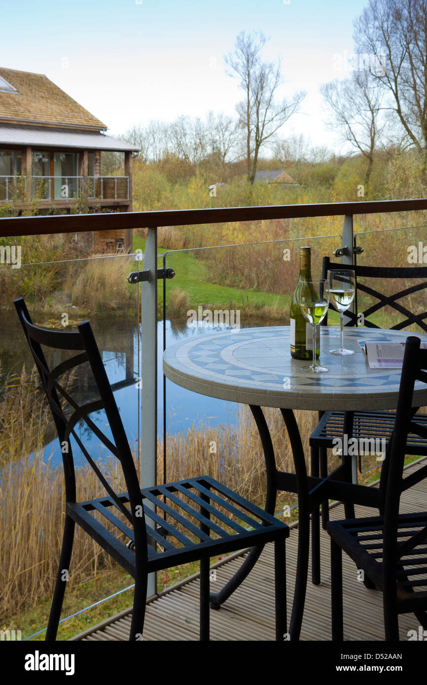 A small outdoor table and chairs on a holiday home veranda with a view of a small lake, Gloucestershire, England, UK Stock Photo