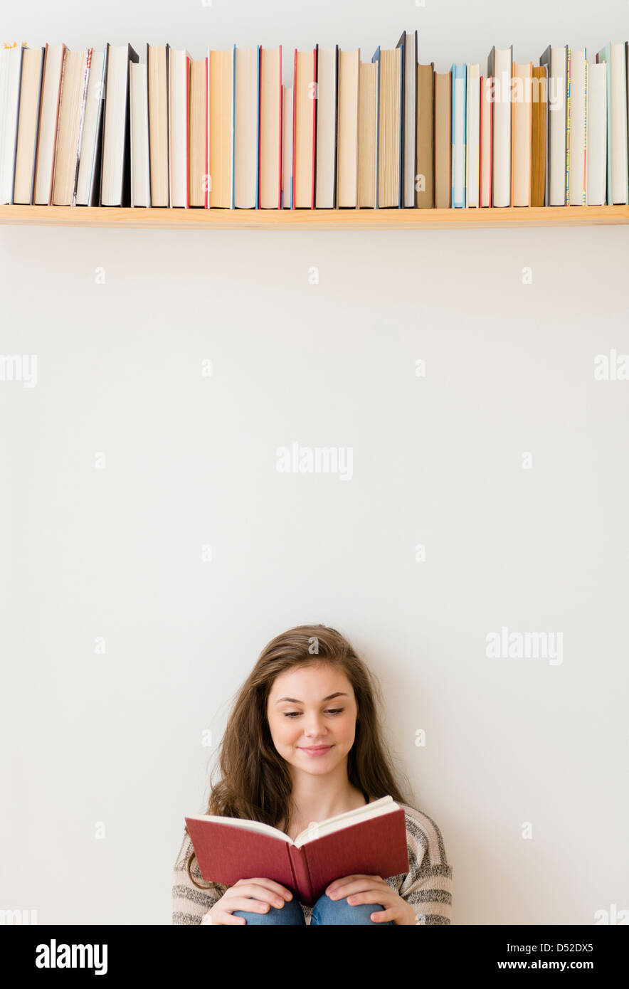 Hispanic girl reading under bookshelf Stock Photo