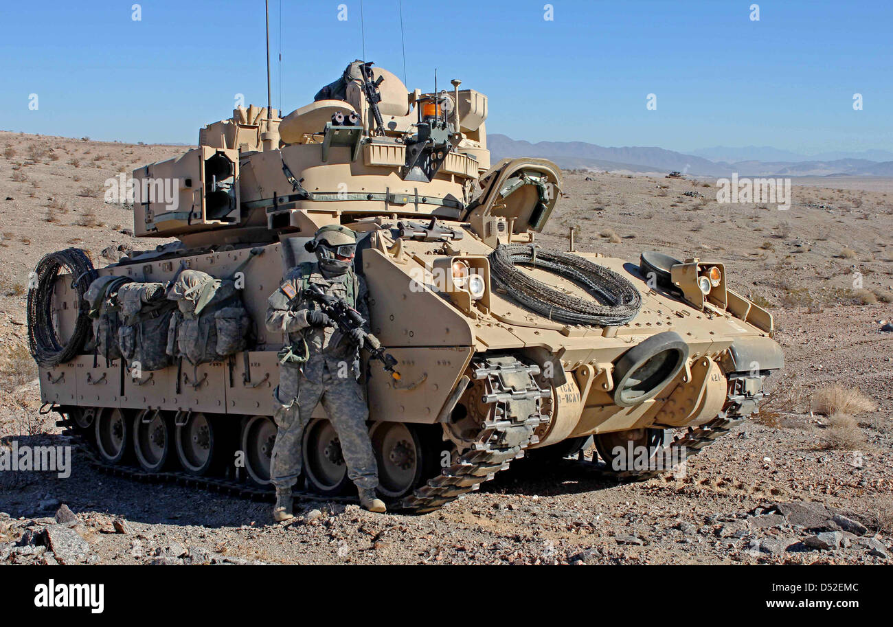 A US Army soldier takes cover next to a M2 Bradley Infantry Fighting