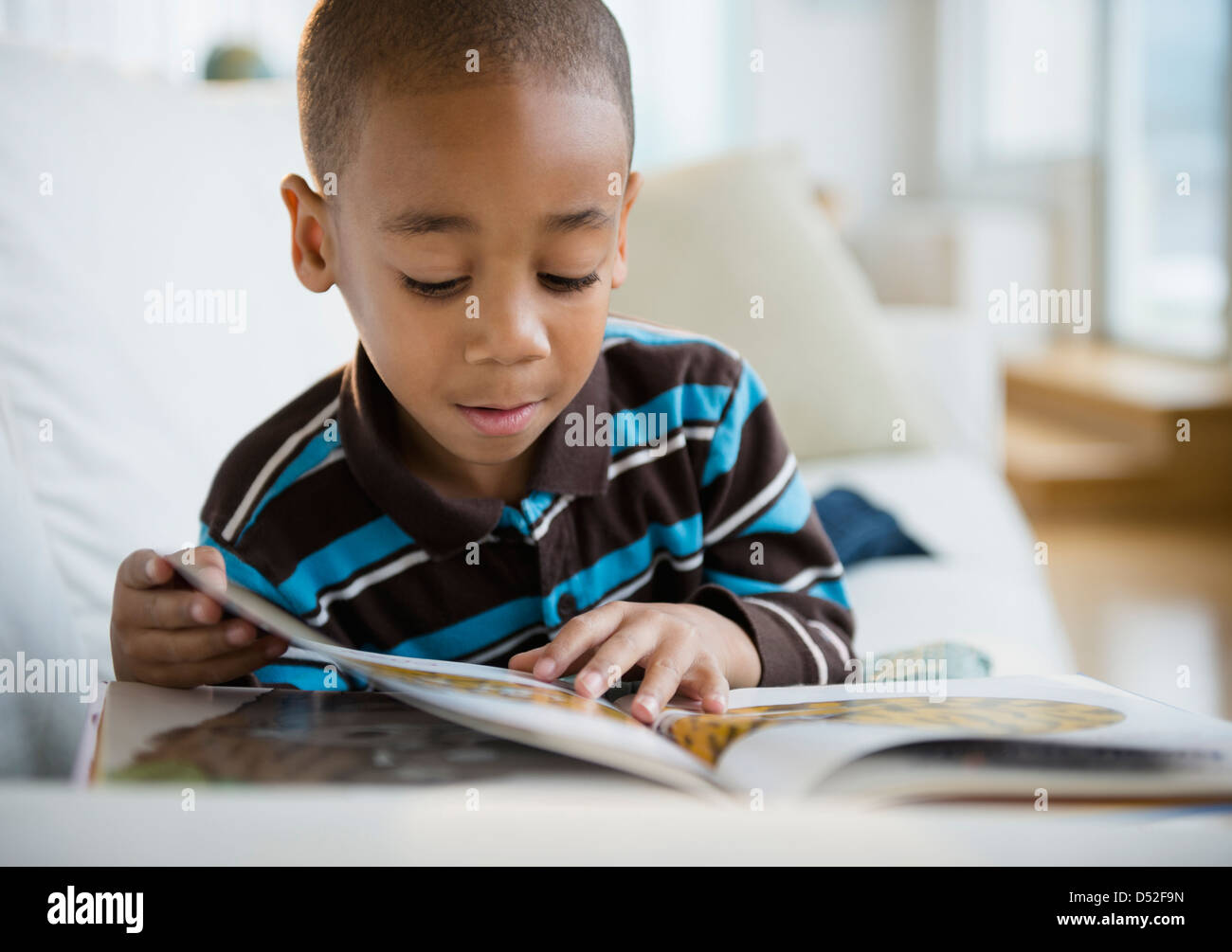 African American boy reading book on sofa Stock Photo