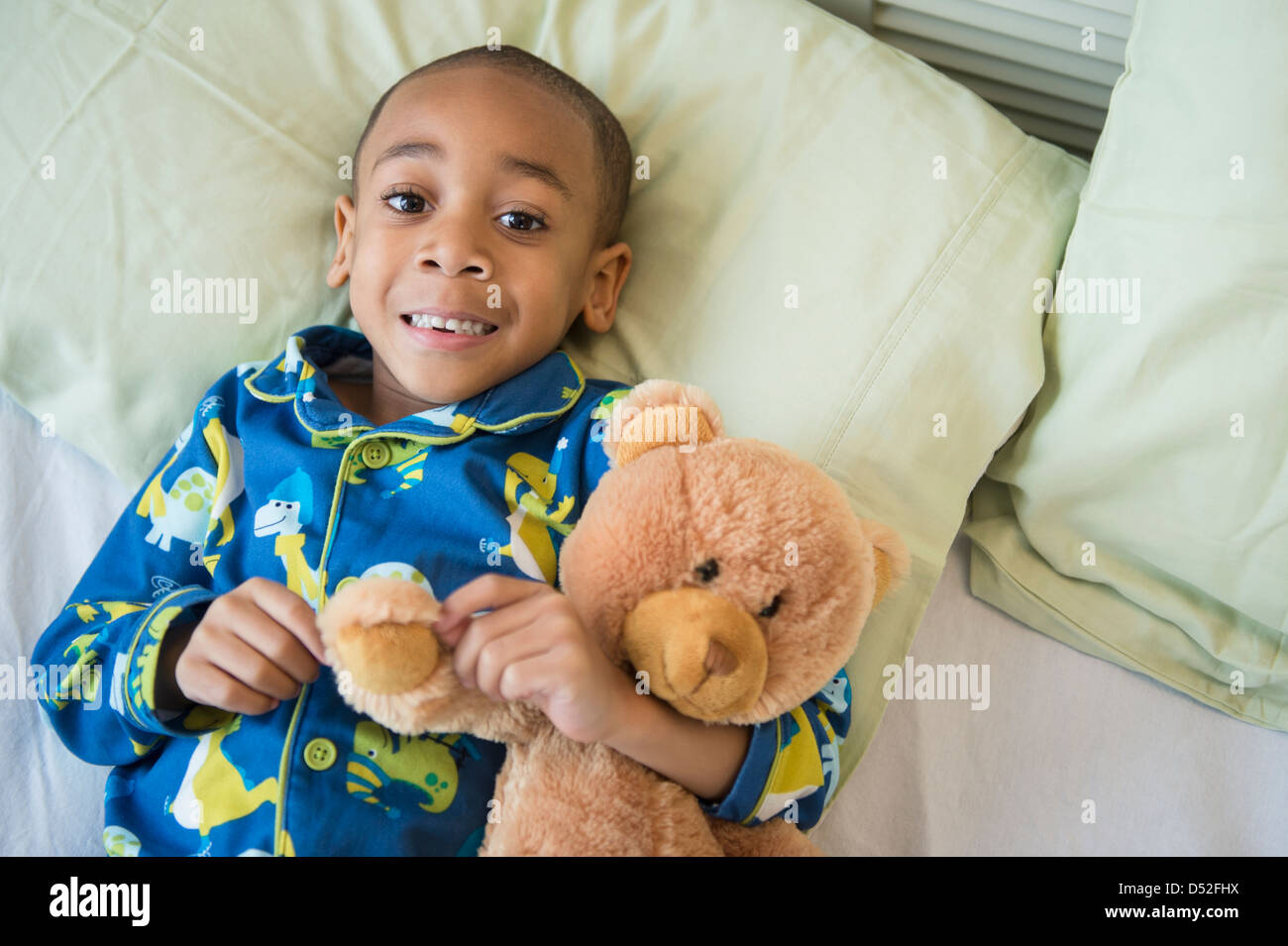 African American boy hugging teddy bear in bed Stock Photo Alamy