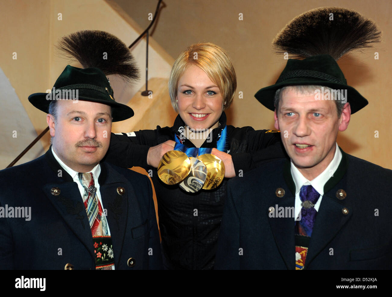 German biathlete Magdalena Neuner poses with her medals next to two men in traditional clothing during the reception in her home town Wallgau, Germany, 05 March 2010. Neuner won two gold medals and one silver medal at the Olympic Winter Games 2010 in Vancouver, Canada and is expected on a specially built stage on the town square in the late afternoon. Photo: TOBIAS HASE Stock Photo