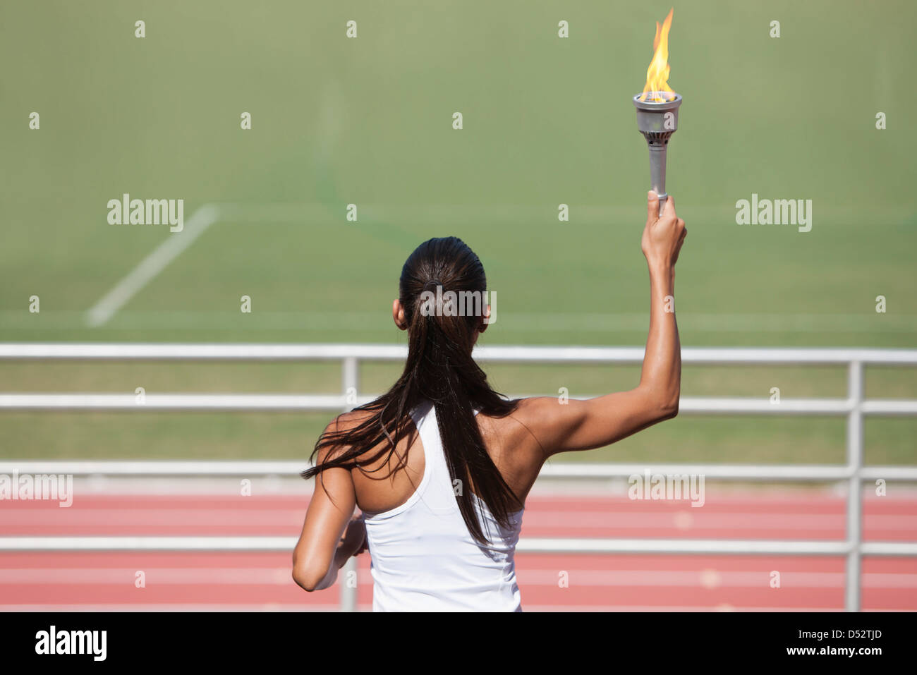 Female athlete holding up flaming torch, rear view Stock Photo