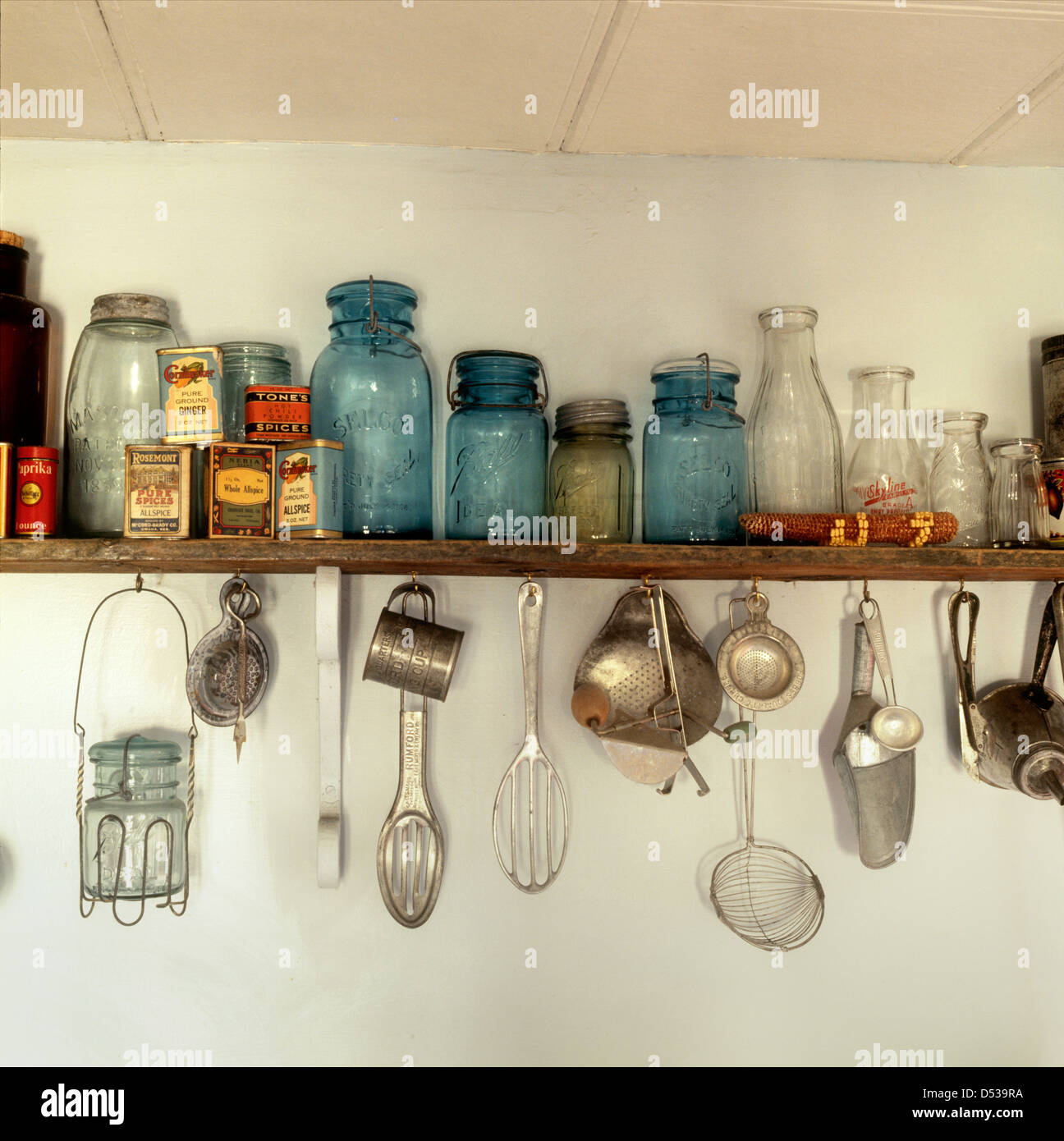 Antique memorabilia kitchen shelf with Mason style jars milk bottles spices and variety of implements. Lincoln Nebraska NE USA Stock Photo