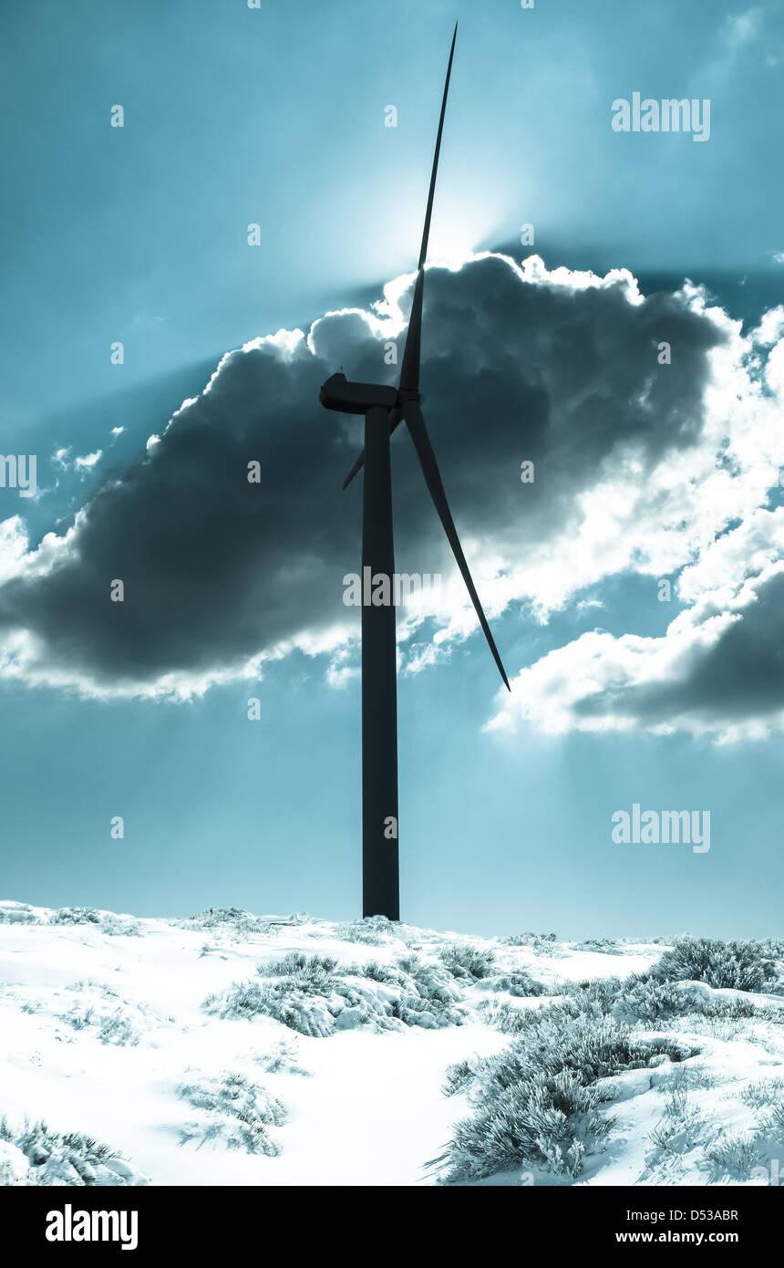 Wind turbine in the back light of the sun with blue sky and clouds on a snow mountain Stock Photo