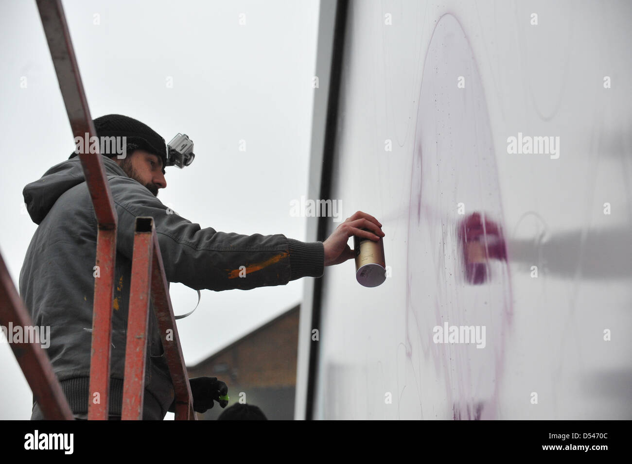 Old Street, London, UK. 24th March 2013. An artist spraypaints onto one of the billboards in Old Street as part of the CALM campaign. Graffiti artists paint on three billboards in Old Street, London for CALM (Campaign Against Living Miserably) to highlight the issue that on average three young men end their lives everyday due to depression and anxiety. Stock Photo